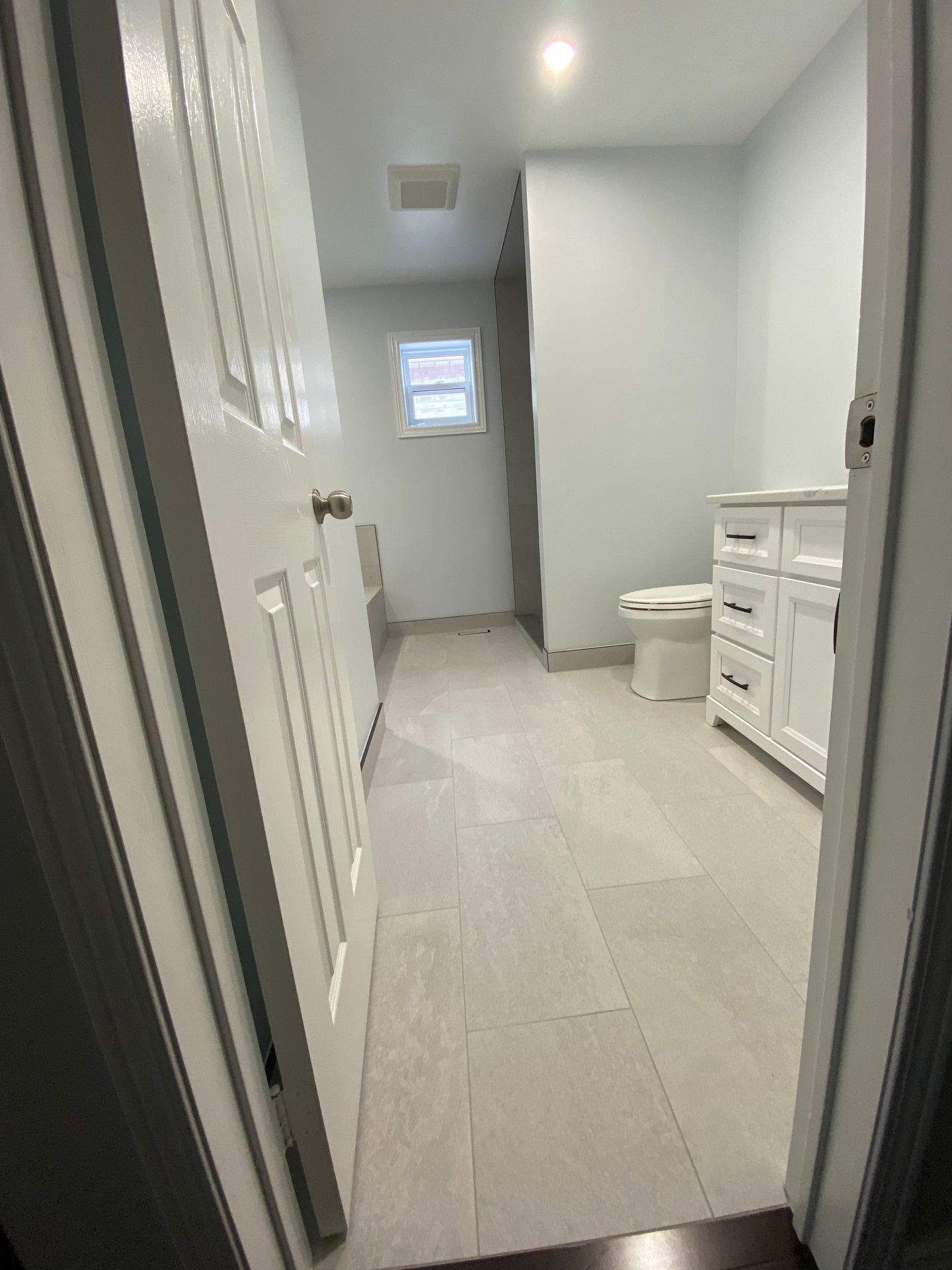 Modern bathroom with large tiles, white fixtures, and a small window above the toilet.