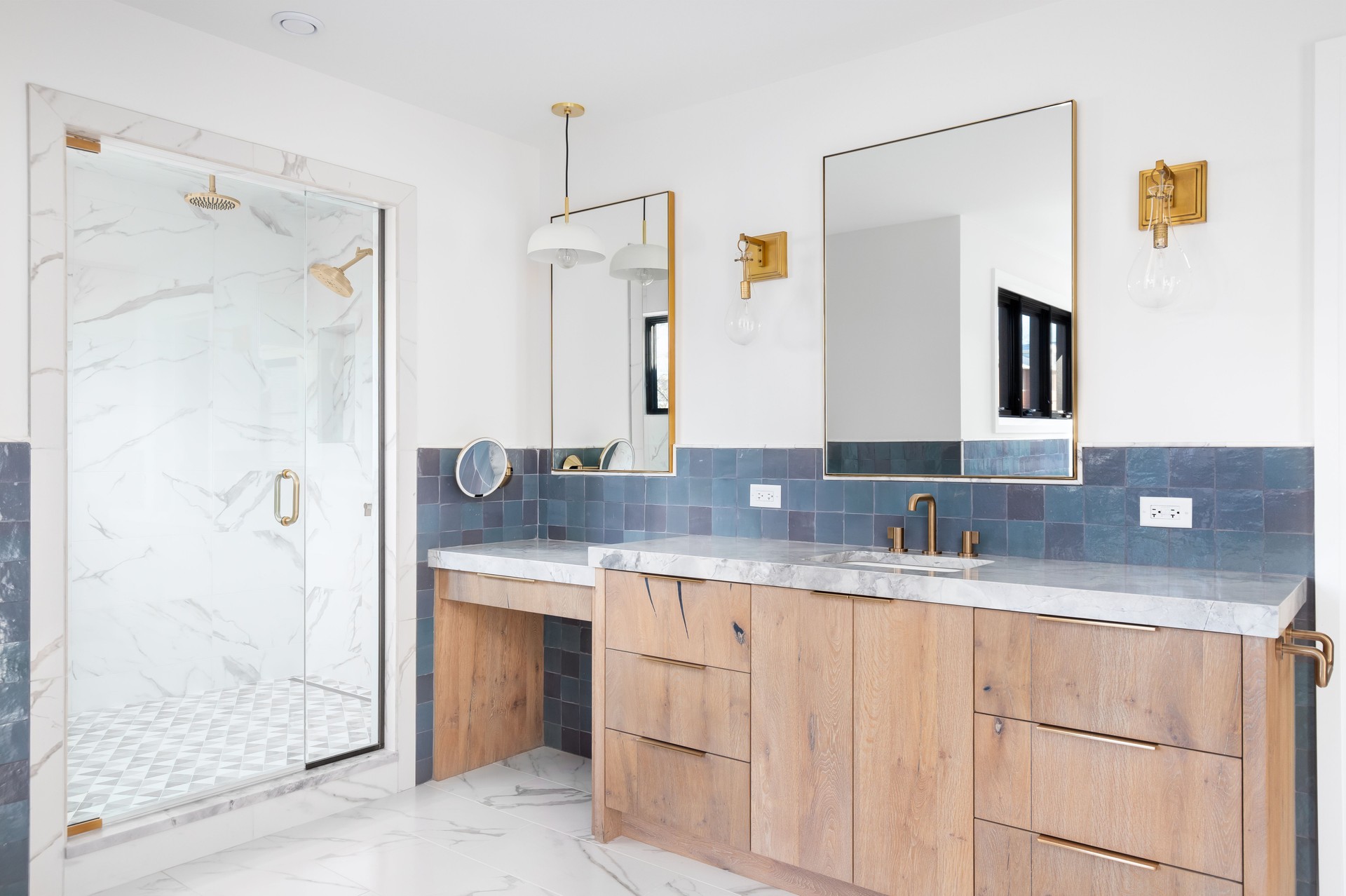 A bathroom with a wood cabinet, gold accents, and a marble shower.